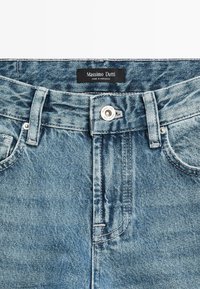Blue denim jeans with a button closure labeled "Massimo Dutti," belt loops, and a black brand label stating "Made in Morocco."