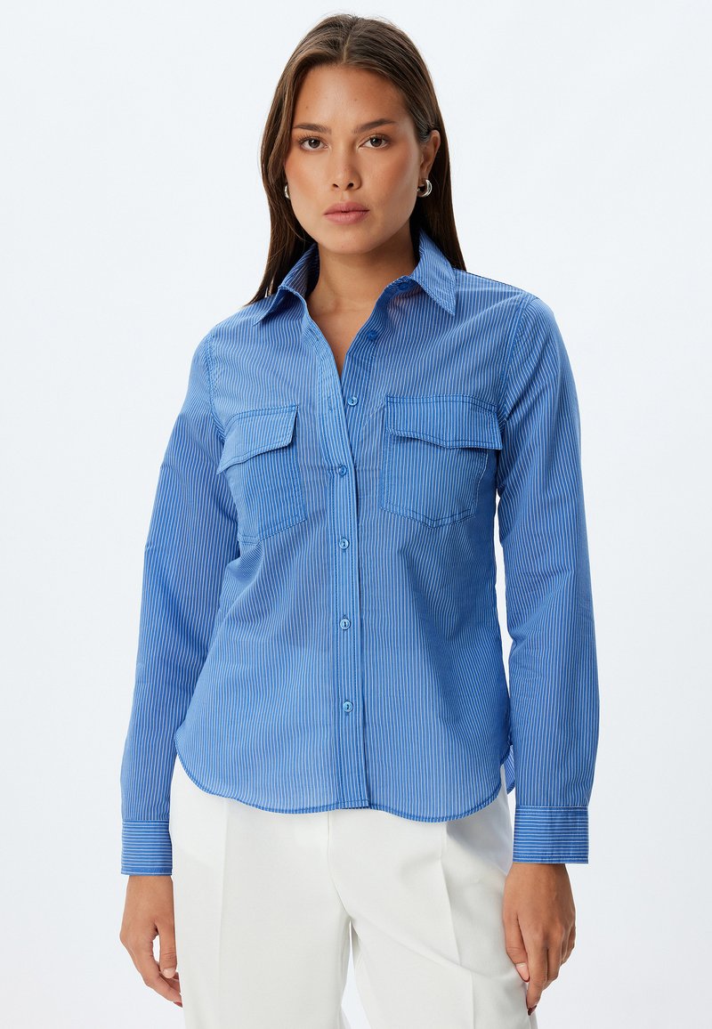 Camisa de botones a rayas azules con manga larga, dos bolsillos en el pecho y cuello extendido; hecha de una tela lisa y ligera.