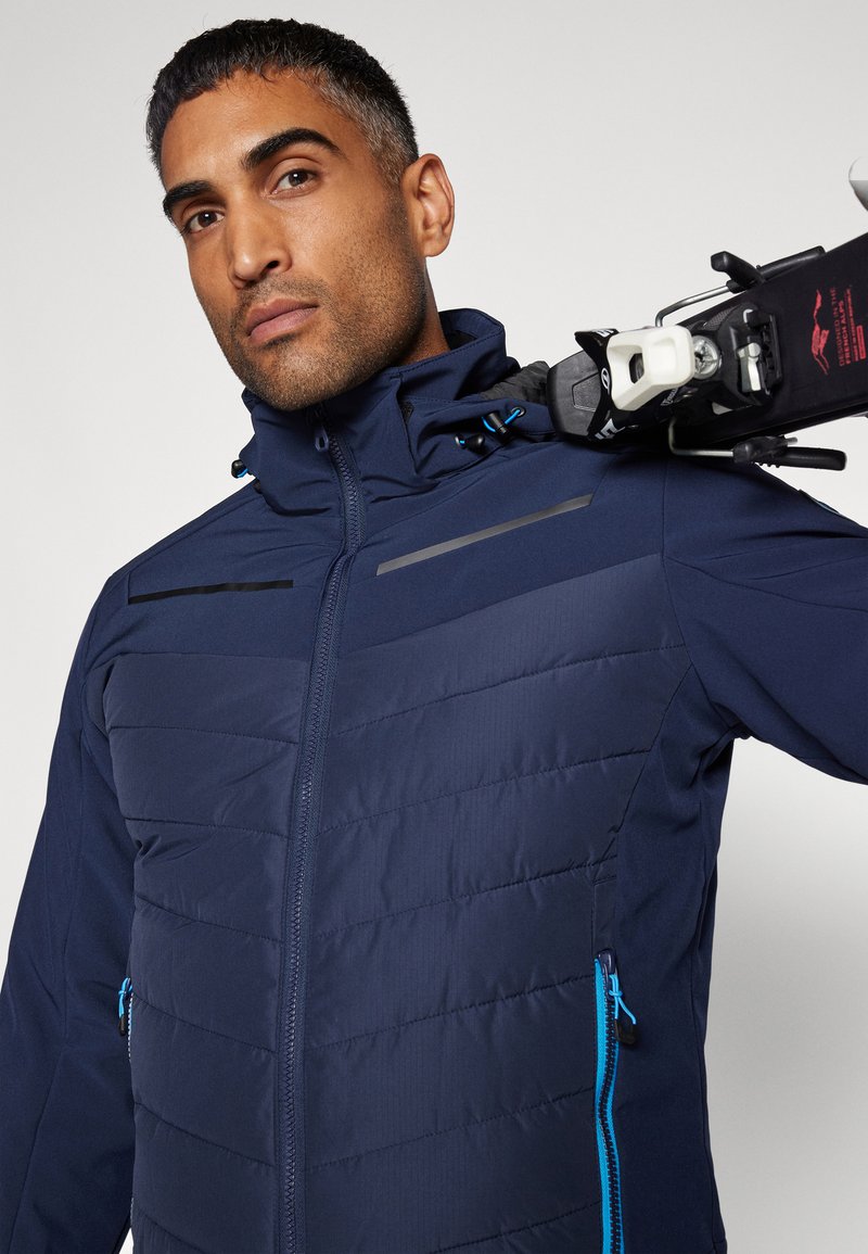 Marine geïsoleerde jas met horizontale quiltstructuur, blauwe ritsaccenten, hoge kraag en harnasbevestiging voor skikleding.