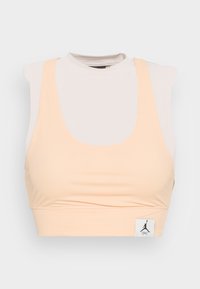 Jasno brzoskwiniowy sportowy stanik z siateczki z okrągłym dekoltem i małą czarną naszywką z logo Jumpman na dolnym brzegu.