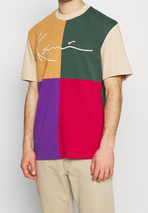 Tričko s blokovými barvami v odstínech hnědé, zelené, fialové a červené. Obsahuje vyšitý bílý logotyp. Vyrobeno z bavlny, krátké rukávy.