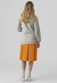 Grå sweatshirt med puffärmar, kombinerad med en orange veckad kjol, texturerade beige strumpor och krämfärgade blockklackade skor.