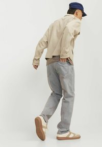 Bež traper jakna preko taupe majice, u kombinaciji sa svijetlo sivoj trapericama i bež tenisicama. Outfit ima opušteni kroj i ležeran dizajn.