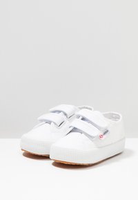 Sneakers bianchi in tela con due strappi in velcro, suola in gomma testurizzata, punta rotonda e logo del marchio ben visibile sul lato.