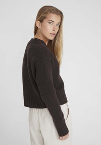 Pull en tricot marron foncé avec ourlet et poignets côtelés, présentant un col en V et une coupe décontractée. Matière douce et texturée qui apporte de la chaleur.