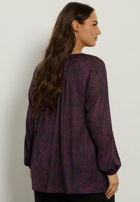 Blusa a maniche lunghe viola e nera con un motivo testurizzato, vestibilità comoda e maniche arricciate. Design minimalista con scollatura rotonda.