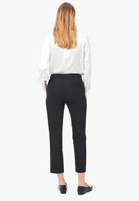 Pantalones negros ajustados con un corte slim y diseño recortado, presentando un acabado suave. Combinados con una blusa blanca de manga larga y zapatos planos.