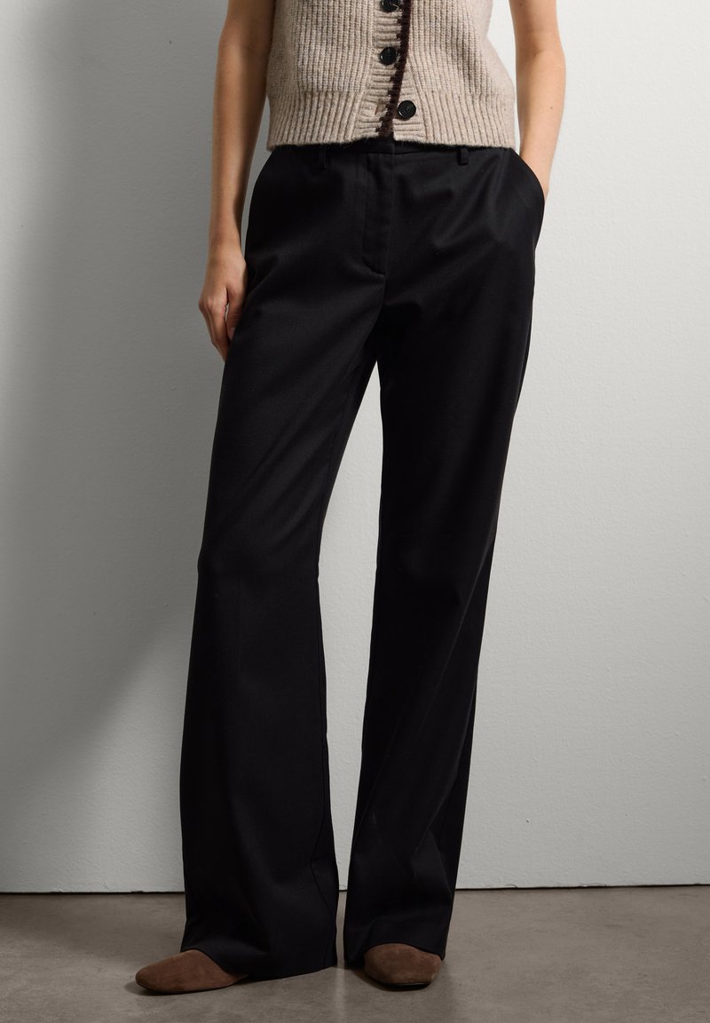 Zwarte op maat gemaakte broeken met een rechte pijp, met een gladde textuur en zijzakken, gecombineerd met een beige geribbelde mouwloze top.