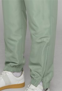 Heleroheline elastse mansetiga püksid külje lukuga pahkluu juures, kantud koos valgete kummipaelte ja valgete sokkidega.