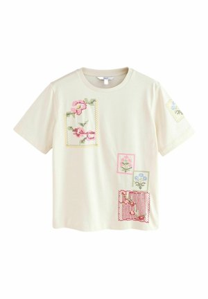 T-shirt en coton crème avec broderie florale multicolore dans un design en patchwork. Manches courtes, col rond, avec divers carrés et rectangles.