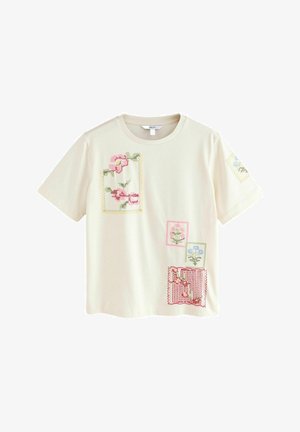 Cremefarbener Baumwoll-T-Shirt mit mehrfarbiger Blumenstickerei im Patchworkdesign. Kurze Ärmel, Rundhalsausschnitt, mit verschiedenen quadratischen und rechteckigen Patches.