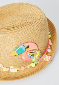 Tannak szalma kalap, színes tukán díszítéssel, neon pom-pomokkal és szív alakú díszekkel az árnyék mentén.