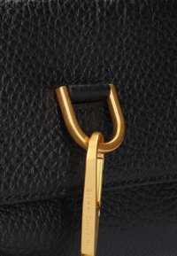 Borsa in pelle nera con texture, caratterizzata da una clip in metallo dorato e accessori. Il pattern della grana notevole aumenta l'interesse visivo.