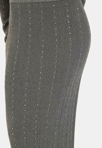 Falda gris con textura de canalé y rayas verticales, que presenta cuentas metálicas distribuidas uniformemente por toda la tela, mostrando un diseño texturizado.
