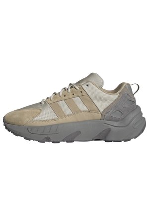 Beige and gray athletic sneaker with mesh and suede panels, three stripes on the side, lace-up closure, and thick textured sole.
