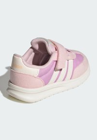 Růžové tenisky s vrchní částí z semiše a syntetického materiálu, suchý zip, bílé tři pruhy a texturovaná gumová podrážka. Měkké polstrování kolem límce.