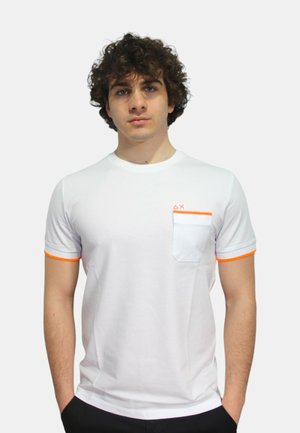 T-shirt bianco a maniche corte con accenti arancioni sulle maniche e nella tasca. Presenta una tasca bianca a contrasto e dettagli nel colletto di colore bianco.