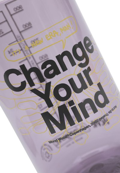 Vijolična steklenica z merilno lestvico. Značilen je poudarjen črn napis "Spremeni svoj um" ter rumen govornični oblaček z napisom "To je nova doba, človek!"