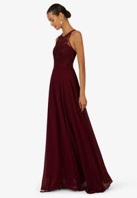 Bordeaux avondjurk met een aansluitend kant lijfje en een vloeiende, gelaagde chiffon rok. Ronde halslijn en mouwloos ontwerp.