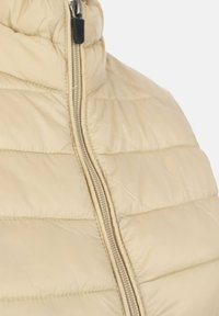 Abrigo puffer beige con un cuello alto y textura suave. Presenta una cremallera frontal completa y un diseño acolchado horizontal.