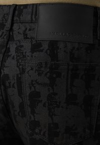 Schwarze Jeansshorts mit einem strukturierten, camouflageähnlichen Muster und einem markierten Lederpatch mit der Aufschrift "Karl Lagerfeld" am Bund.