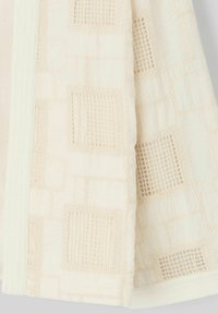 Tissu beige texturé avec des motifs en grille tissés ; présente des coutures subtiles et un bord lisse ; matériau léger et respirant.