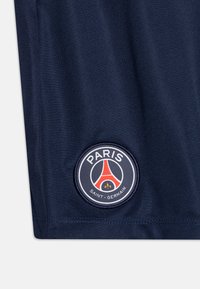 Tmavomodrá látka s hladkou textúrou, s kruhovou nášivkou v červenej, bielej a modrej farbe, na ktorej je nápis "PARIS SAINT-GERMAIN".