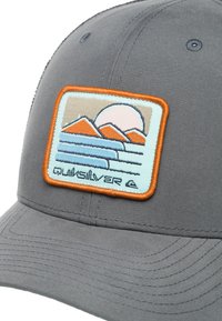 Gray cap with a structured crown and curved brim. Features a rectangular patch with an embroidered mountain and sunset design in orange, blue, and beige.