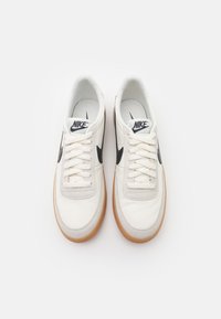 Nike αθλητικά παπούτσια με λευκό δερμάτινο πάνω μέρος, γκρι σουέτ λεπτομέρειες, μαύρο λογότυπο swoosh και σόλα από καουτσούκ γκοφρέ. Ισιωμένες κλωστές και μαλακό κολάρο.