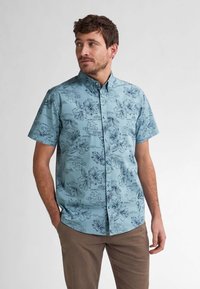 Camisa de manga corta, abotonada, en azul claro con patrones florales en azul oscuro. Presenta un cuello clásico y un corte relajado.