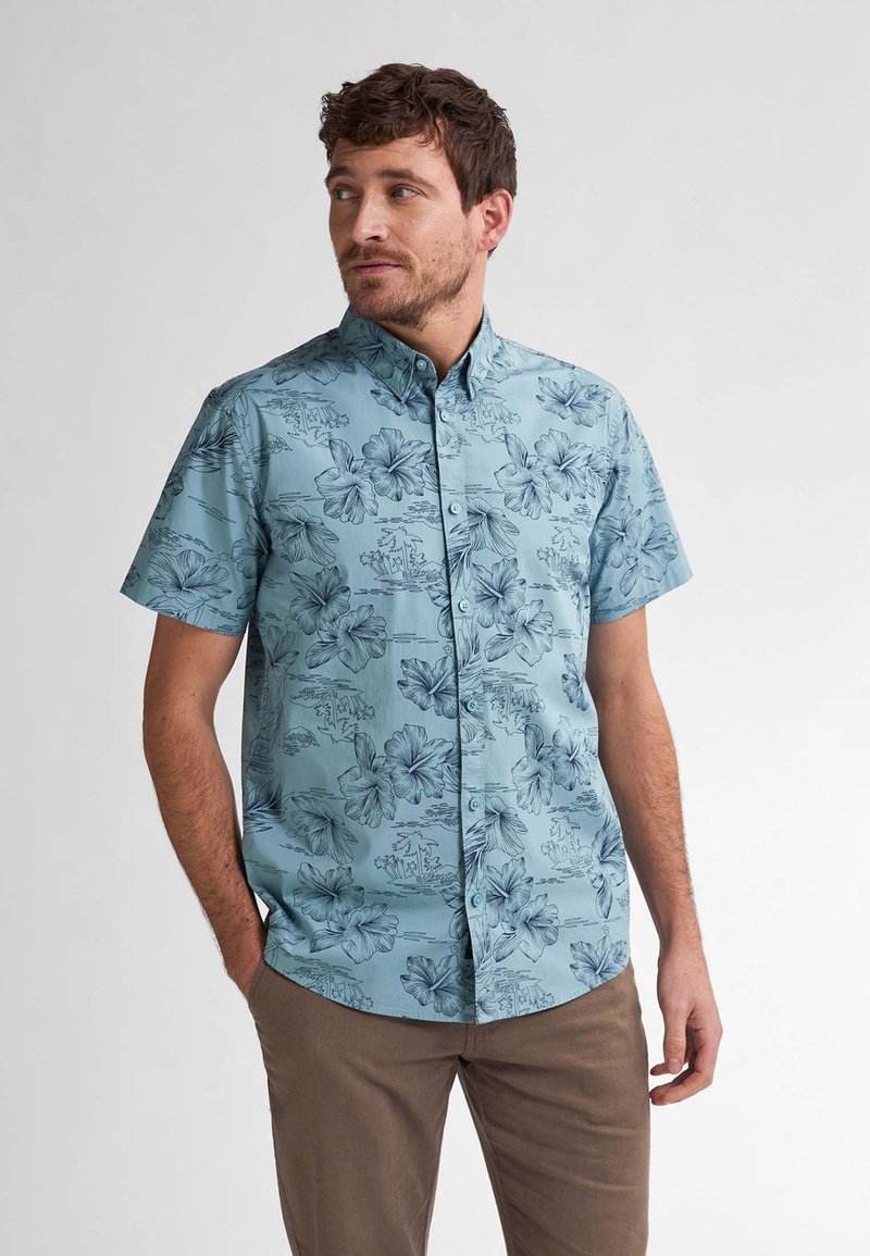 Camisa de manga corta, abotonada, en azul claro con patrones florales en azul oscuro. Presenta un cuello clásico y un corte relajado.