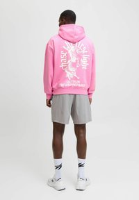 Sudadera con capucha rosa con gráficos blancos en la parte posterior, combinada con pantalones cortos grises. Presenta un corte cómodo y una tela suave.