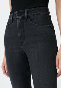 Jeans en denim noir à coupe slim, taille haute et poches avant. Présente une fermeture à bouton et une texture subtile dans le tissu.