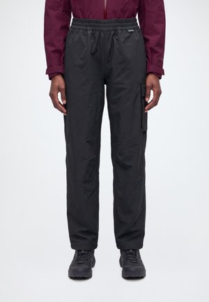 Un mannequin porte un pantalon cargo noir à coupe ample, avec une taille élastique et une poche latérale, associé à une veste bordeaux et à des chaussures noires.