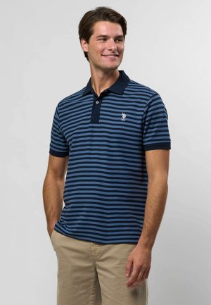 Randig pikétröja i marinblått och blått med en kontrasterande krage, korta ärmar och broderad logotyp på bröstet. Tillverkad av ett mjukt tyg.