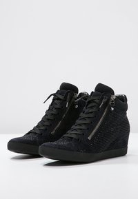 Des baskets compensées en daim noir présentent un laçage à l'avant, des fermetures éclair sur les côtés et des détails en clous métalliques sur le dessus. Talon compensé texturé.