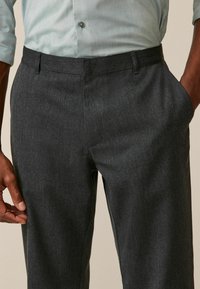 Pantalon ajusté gris foncé en tissu texturé, avec des poches latérales et une coupe flat front. Détails en matériau doux visibles.