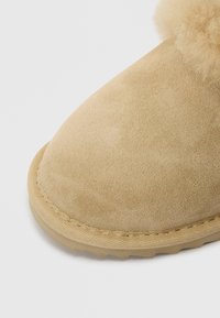 Tan mockaskinnboots med rund tå, som har en texturerad yta och mjuk syntetpäls vid öppningen. Sytt mönster längs sulan.