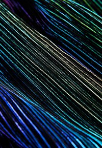 Il materiale presenta fili sottili, lucidi e iridescenti in diverse tonalità di nero, verde e blu, creando un aspetto testurizzato e stratificato.