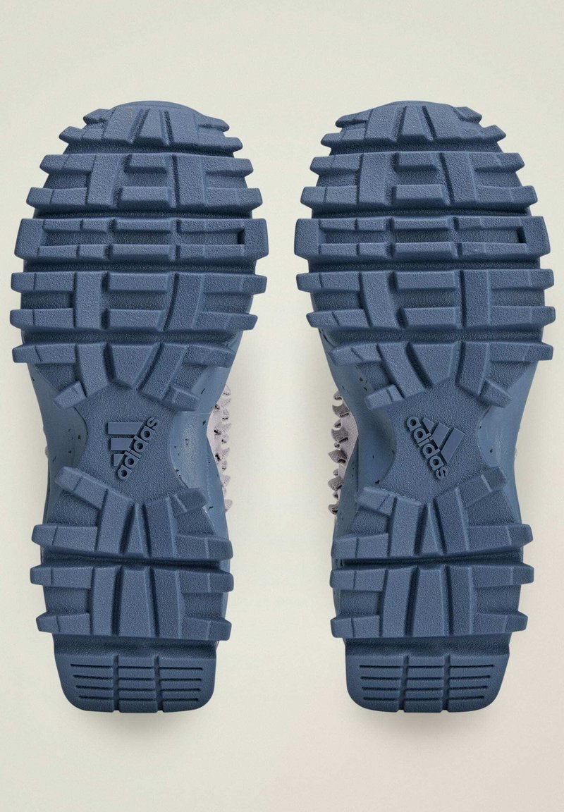 Sottili delle scarpe sportive Adidas con battistrada profondo e irregolare; colore blu; superficie texturizzata; logo prominente su ogni suola.