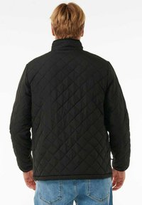 Black quilted jacket with a high collar and diamond pattern on the fabric, displayed from the back, paired with blue jeans.