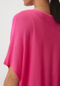 Top in maglia rosa con maniche corte e larghe. Il tessuto è leggero con una texture liscia, presenta un collo rotondo e una vestibilità rilassata.