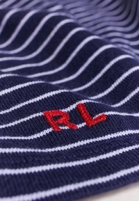 Marineblaues Material mit weißen Streifen, das ein gesticktes rotes "RL"-Logo zeigt. Die Textur wirkt weich und gewebt.