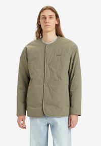 Quilted green jacket with rounded neckline, snap buttons, and subtle LEVI'S logo. Pairs with light blue denim for a casual look.