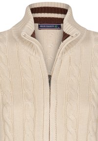 Cremefarvet strikket sweater med høj krave, der har et kabelstrik mønster og en kontrasterende brun og hvid stribet kant ved udskæringen.
