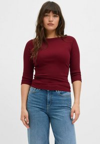 Burgundy ribbad pitkähihaine toppi, jossa on venetsialaiskaula-aukko, yhdistettynä vaaleansinisiin korkeavyötäröisiin farkkuihin. Suora pinta, istuva siluetti.