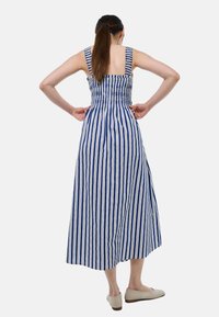 Robe midi rayée bleu et blanc avec un corps smocké, de larges bretelles et une jupe fluide, associée à des chaussures de couleur claire.