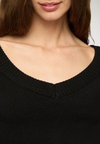 Czarny dzianinowy sweter z głębokim dekoltem w kształcie litery V, z prążkowaną teksturą wzdłuż krawędzi i gładkim przodem. Zbliżenie na okolice dekoltu.