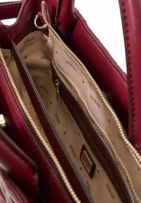 Sac à main bordeaux avec extérieur en cuir synthétique lisse. L'intérieur est doté d'une doublure beige avec le logo de la marque en motif répété, des compartiments zippés et des emplacements pour cartes.