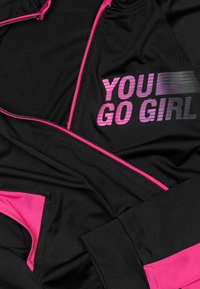 Black athletic jacket with pink accents. Features "YOU GO GIRL" in bold, gradient text. Smooth texture, zippered closure, and fitted design.